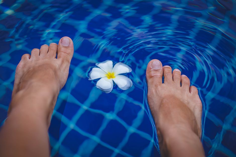 Close-up of feet in a clear blue swimming pool with a floating tropical flower