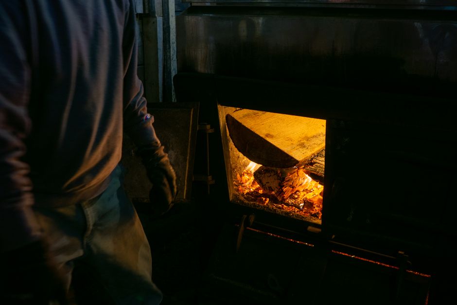 Person tending to a wood fire in a dimly lit room, adding logs to the flames
