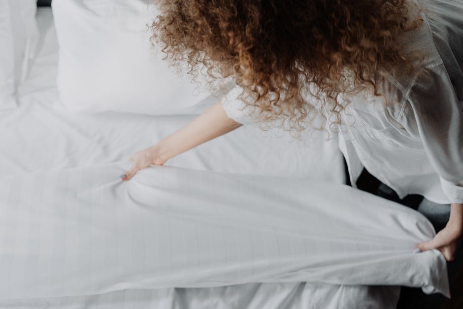 A person arranging white bed linens in a serene bedroom, focusing on clean and cozy atmosphere