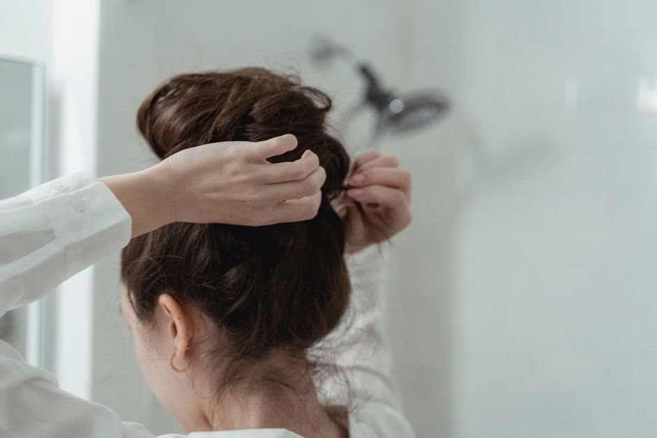 A woman styles her hair into an elegant bun in a bathroom setting, focusing on hair care