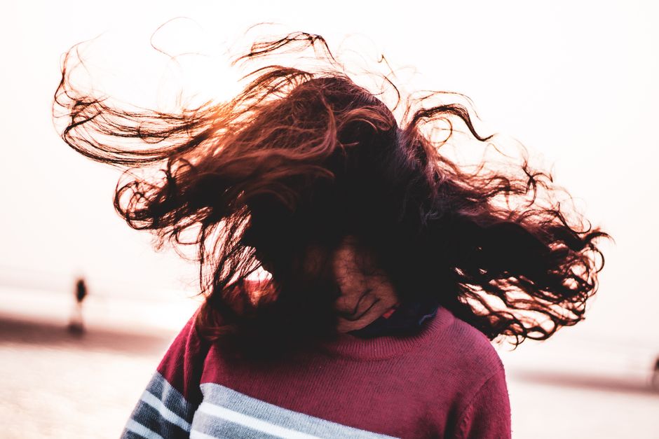 Anonymous female in sweater shaking head with long dark hair while standing on embankment near sea against blurred background