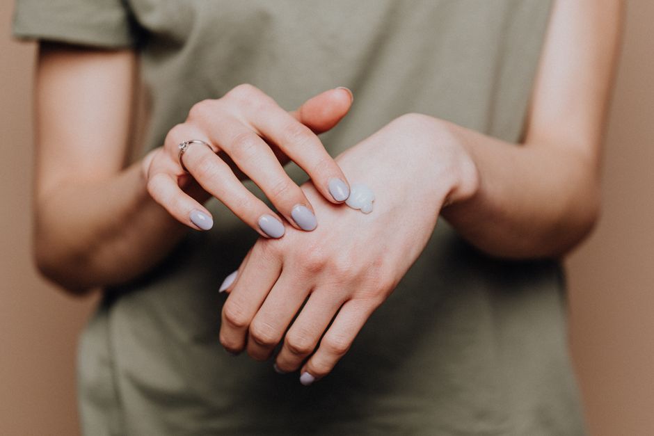 Anonymous female in casual shirt with manicured hands and ring softly rubbing hand moisturizer in back of hand skin
