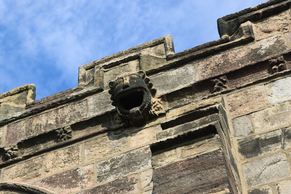 Close-up of a medieval gargoyle on an old English stone castle under a blue sky