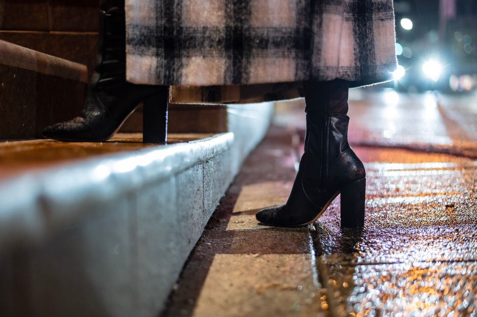 Side view of crop anonymous female in leather boots and checkered coat strolling on staircase in evening town