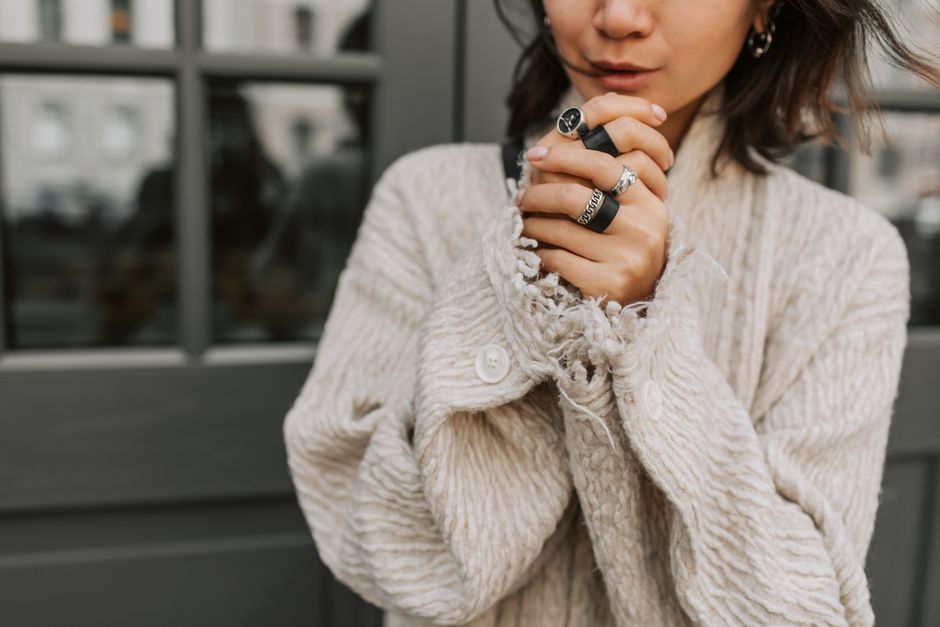 Close-up of a woman clasping hands adorned with rings and a beige coat