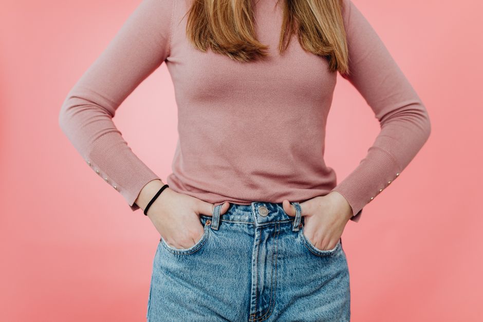 Fashionable woman in pink top and jeans with hands in pockets against pink background