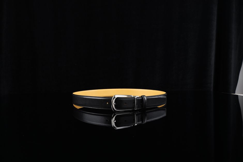 Sophisticated black leather belt with a silver buckle, displayed on a reflective surface against a dark background