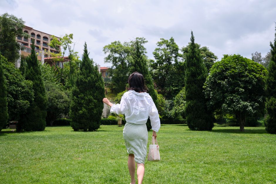 A woman in a green midi skirt walking through a lush park