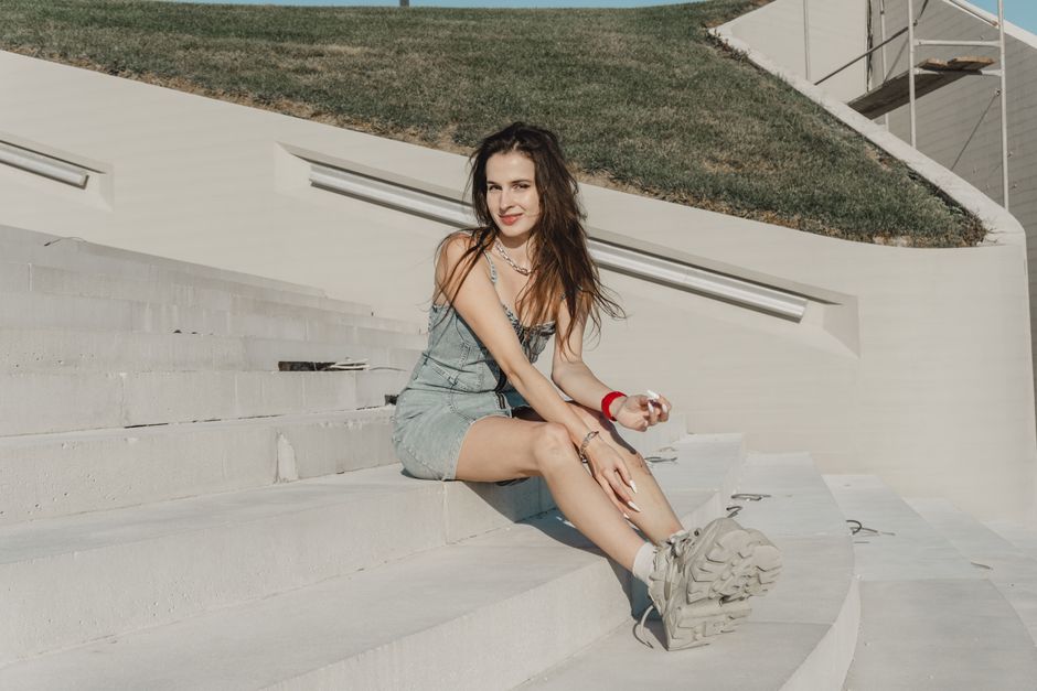 A woman in a denim outfit sits on white concrete stairs under the sun