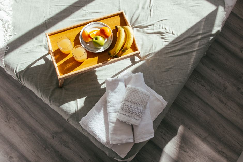 A sunlit bedroom featuring a fresh fruit breakfast tray and neatly folded towels on a soft bed