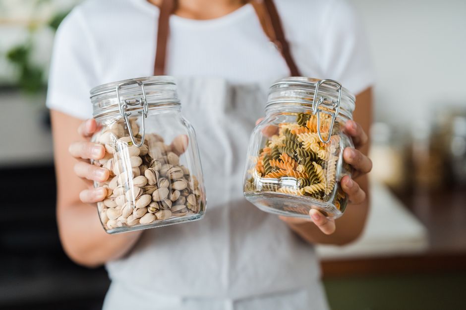 Hands holding glass jars filled with pistachios and colorful spiral pasta indoors
