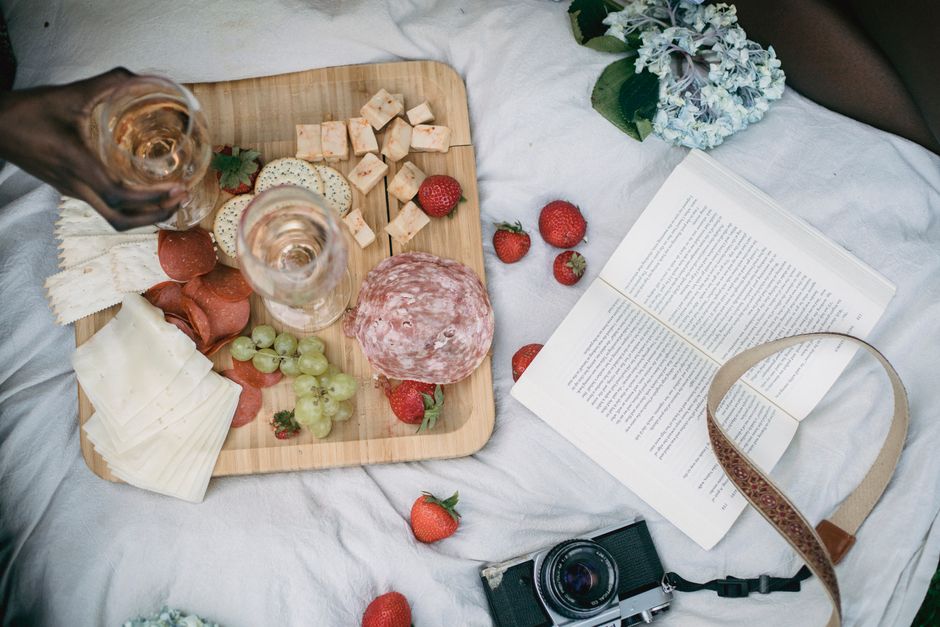 A top-down view of a picnic with charcuterie, wine, and a book outdoors