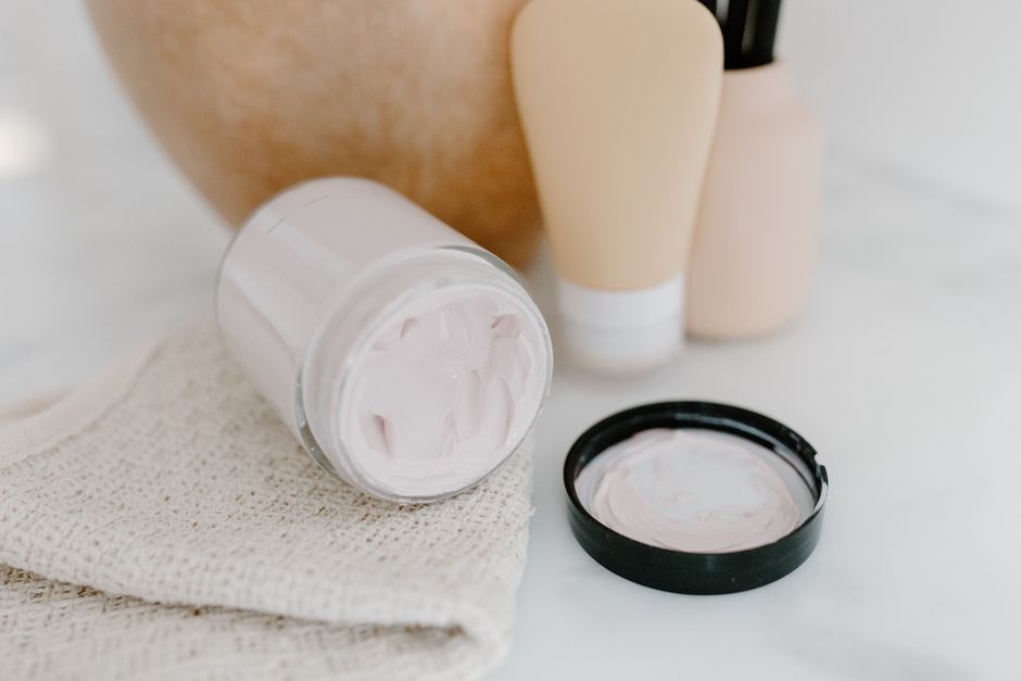 Glass jar with face cream amidst gentle skincare products on a neutral background