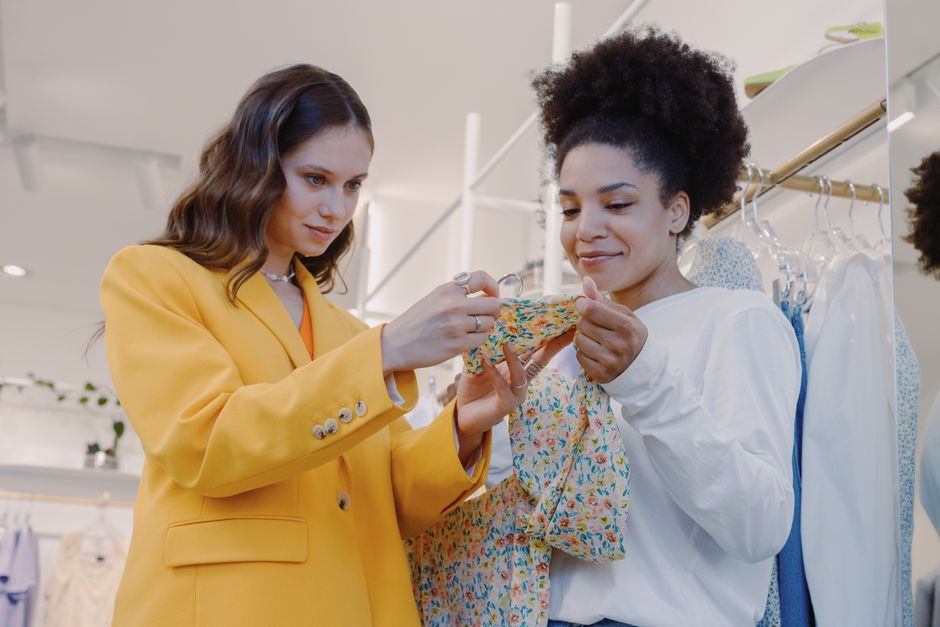 Two women shopping fashionably at a boutique, choosing colorful dresses indoors