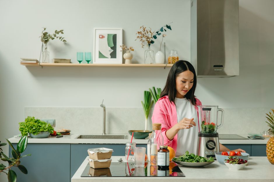 Asian woman blending fresh fruits and vegetables in a stylish kitchen setting