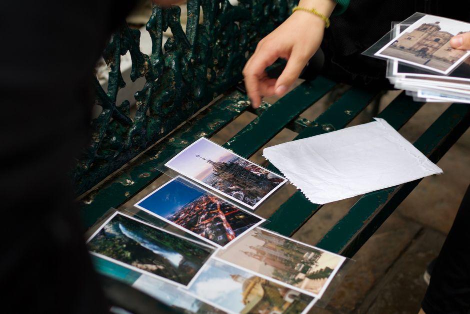 Person choosing travel postcards on ornate bench in outdoor setting