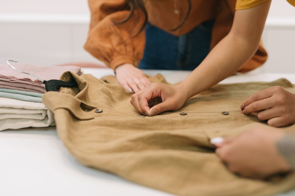 Hands inspecting the details of a beige button-down garment