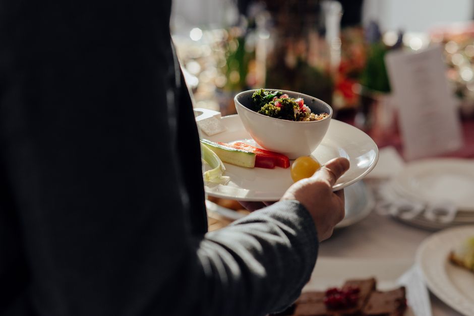 Faceless male with bowl of bulgur with spinach and pomegranate seeds on white plate with cut vegetables standing neat table