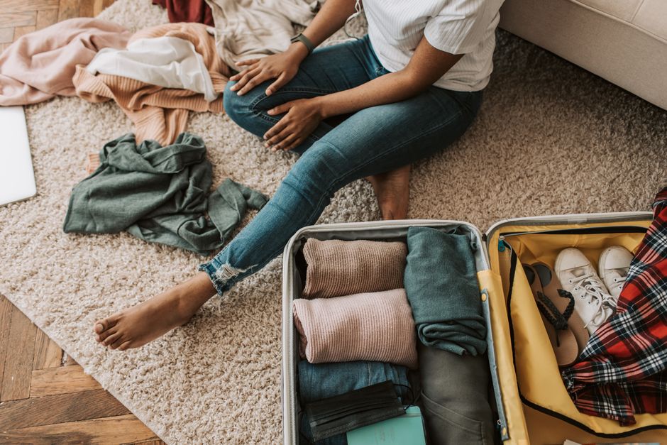 Woman organizing clothes while sitting on floor with open suitcase, preparing for a trip