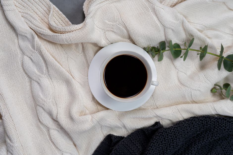 A cozy setup featuring black coffee on a cable knit blanket with green accents