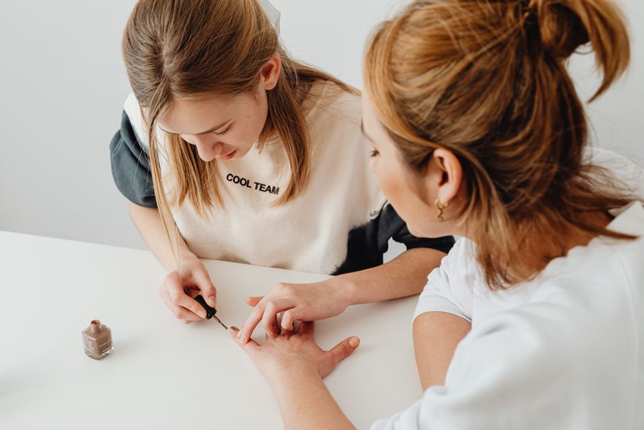 A young woman performs a manicure on another in a well-lit room