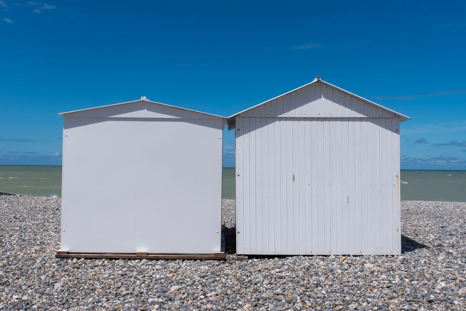 Two white beach huts on a pebble beach with clear blue sky