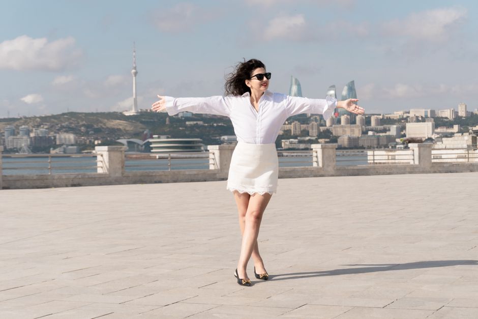 Young woman in a white shirt dress with arms outstretched by the waterfront