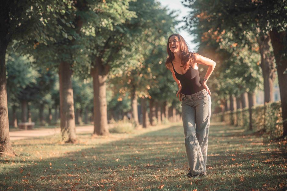 Woman laughing during a walk in a sunlit park surrounded by trees