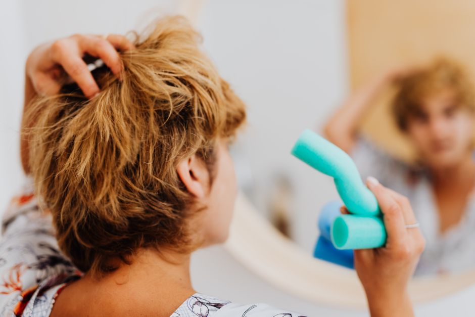 Woman using blue curlers in front of a mirror for daily hair routine