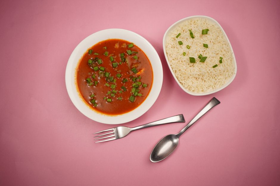 A vibrant flat lay of tomato soup and rice garnished with chives on a pink background
