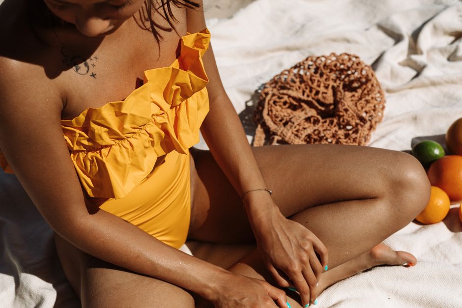 Woman in yellow swimsuit enjoying a sunny day on the beach, sitting on a towel with fruits