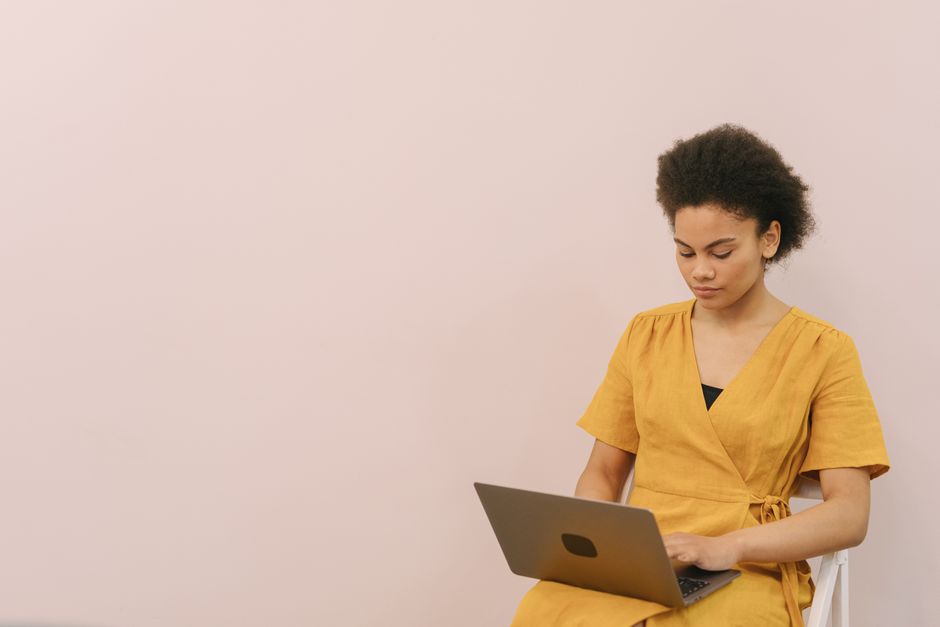 Woman in a mustard yellow top working on a laptop indoors