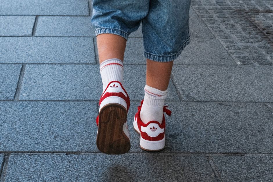 Rear view of person walking in red sneakers and jeans on urban pavement
