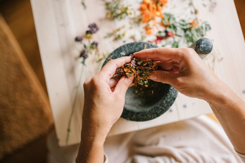 Close-up of hands mixing dried herbs with a mortar and pestle for herbal medicine preparation