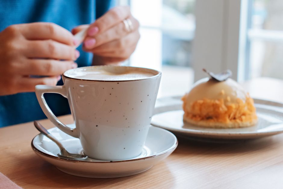 A close-up of a coffee cup and cake on a table in a cozy cafe setting